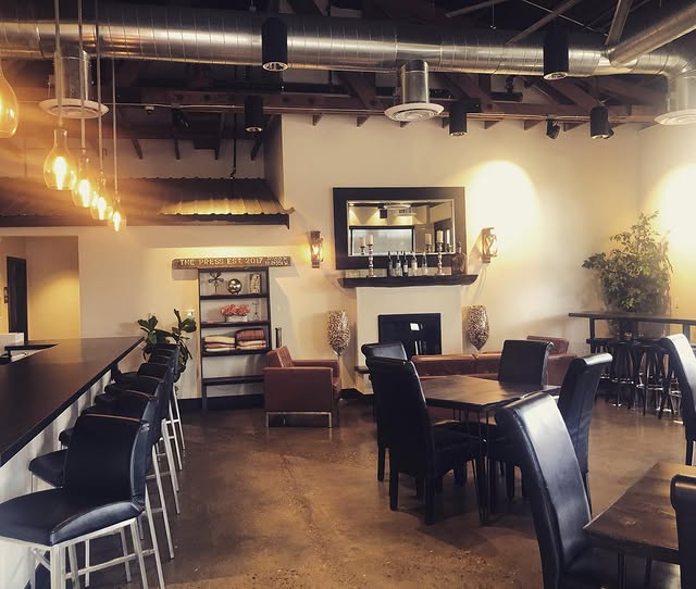 The cozy, warm-lit interior of The Press wine bar with Edison bulbs, leather seating, and a fireplace